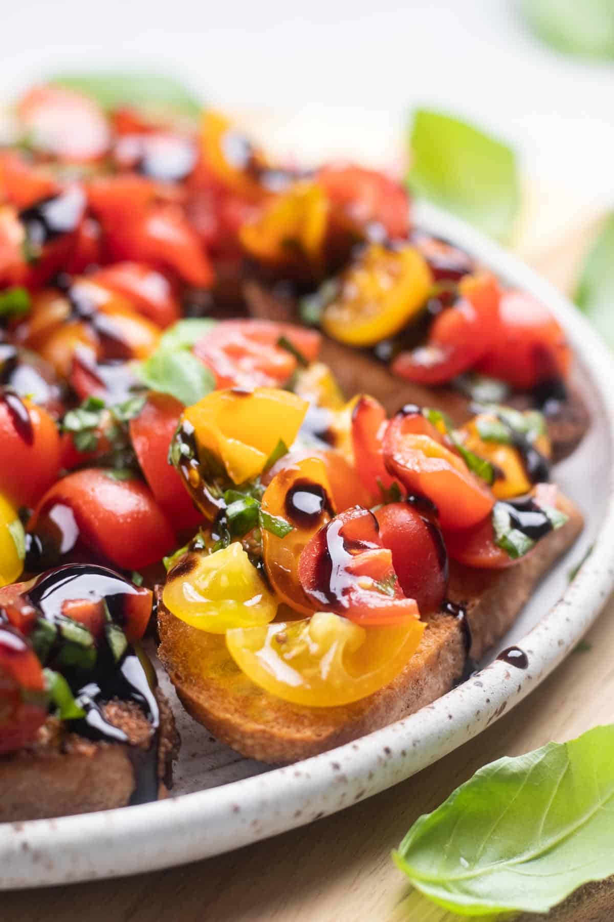 Cherry tomato bruschetta drizzled with balsamic glaze on a white plate.