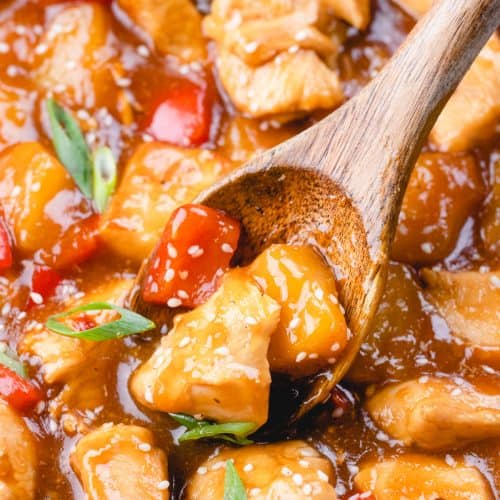 A colse up photo of Hawaiian chicken with a wooden spoon, sprinkled with ssame seeds and green onion.