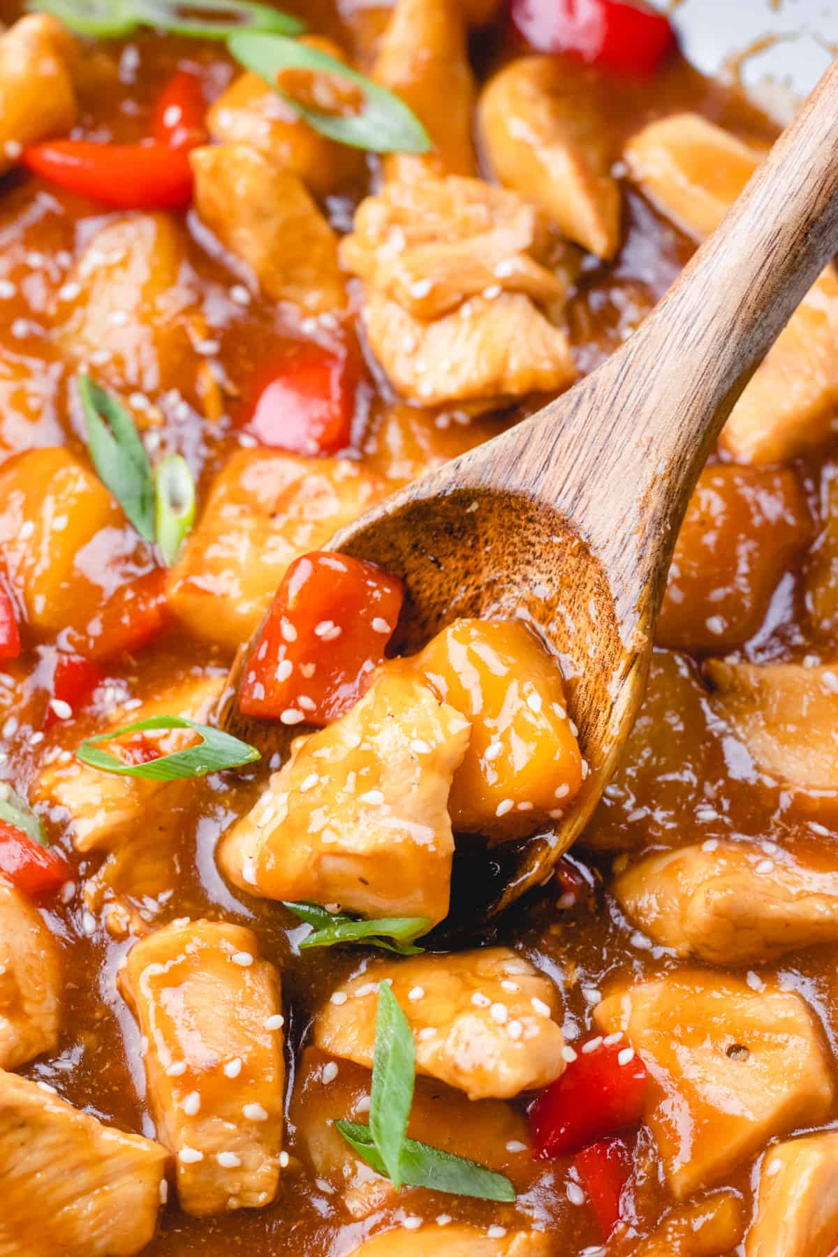 A colse up photo of Hawaiian chicken  with a wooden spoon, sprinkled with ssame seeds and green onion.