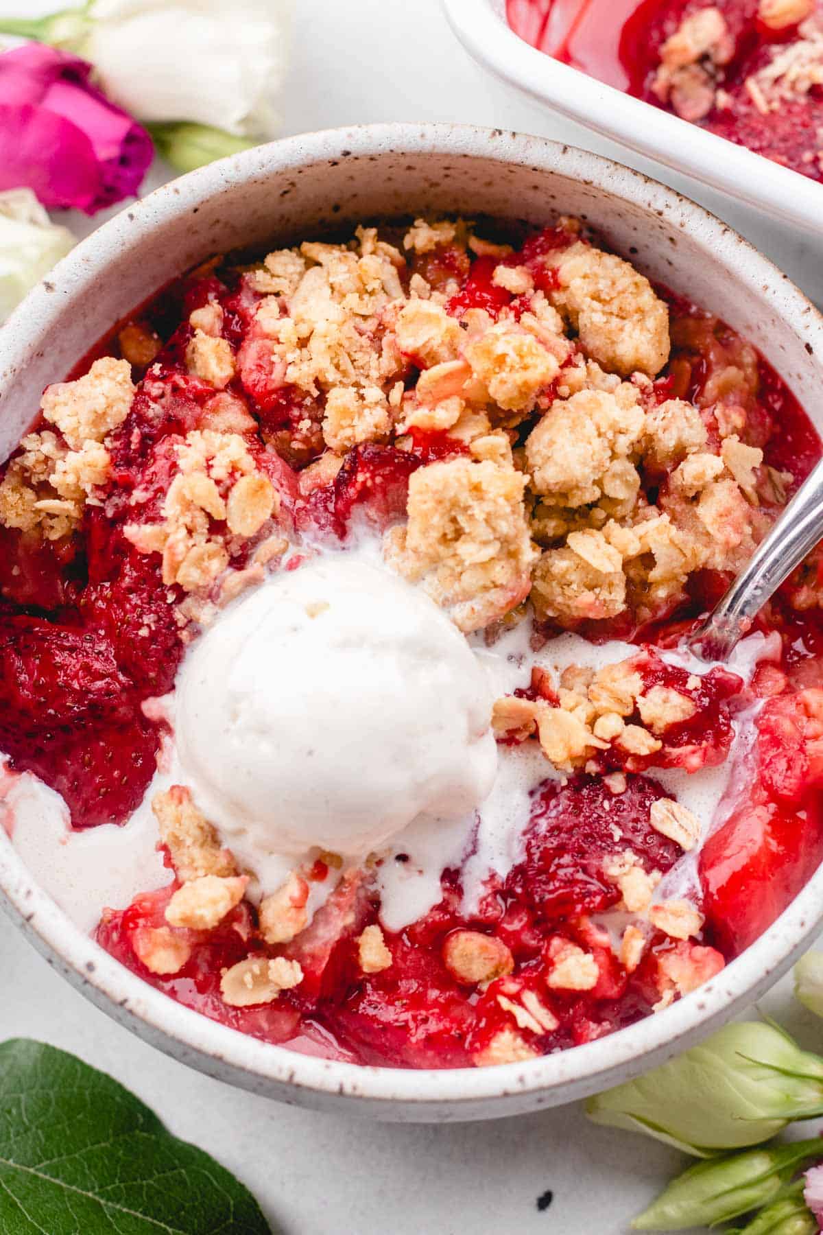 Scooping out strawberry crumble with a spoon, topped with ice cream.