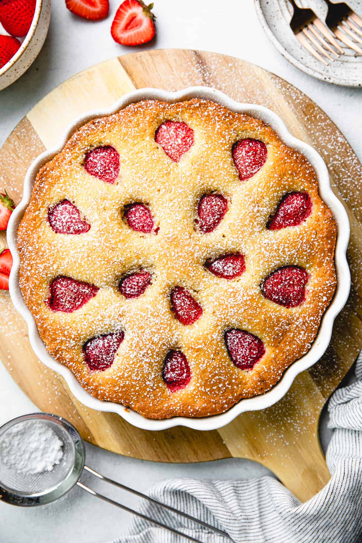 A vanilla coffee cake, topped with strawberries, in a white round baking pan on a wooden board.