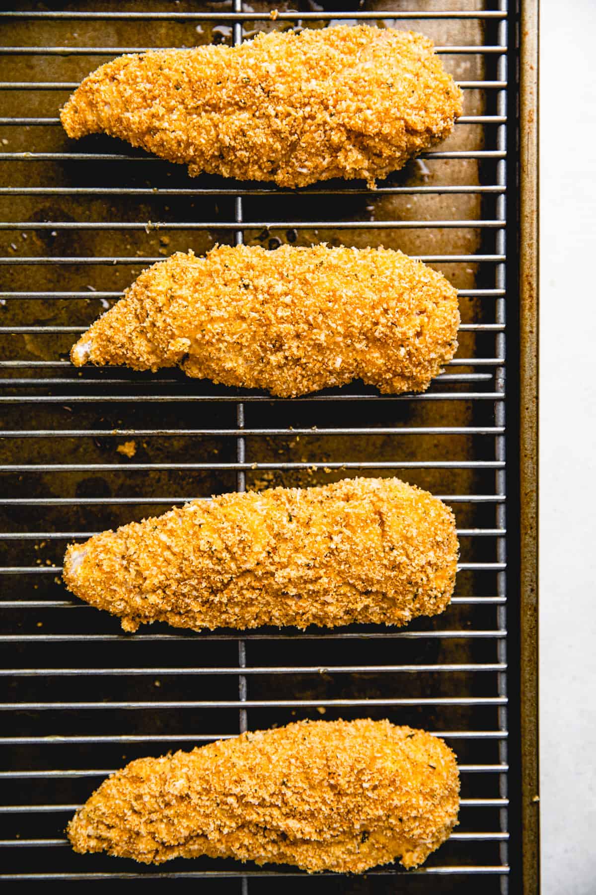 Chicken tenders, coated with breadcrumbs, on a baking sheet with wire rack.