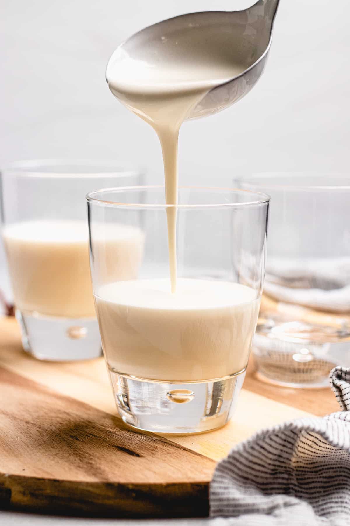 Pouring panna cotta in a glass on a wooden cutting board.