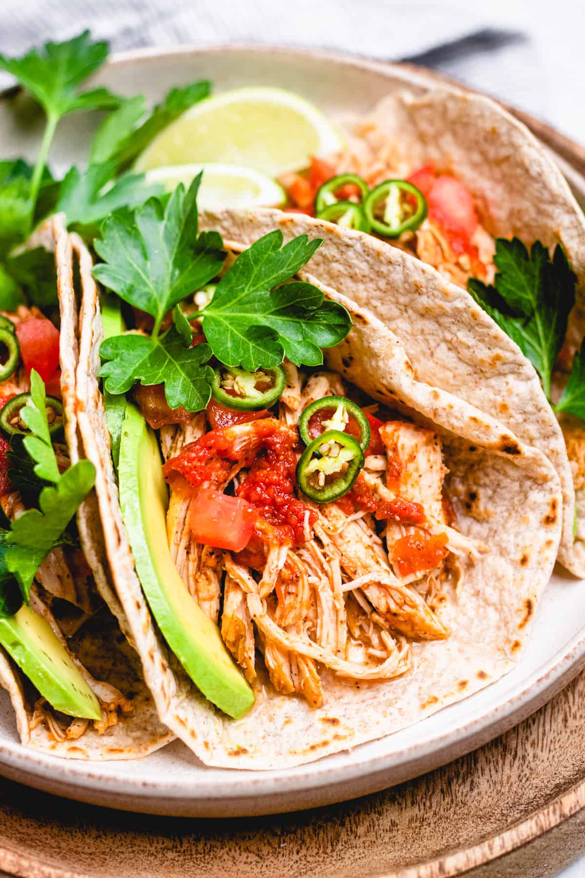 Tacos with shredded chicken, tomatoes, avocado, jalapeno, and cilantro on a plate.