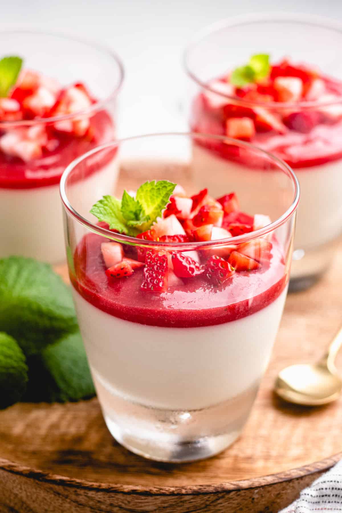 3 glasses with Panna Cotta topped with strawberry sauce on a wooden tray.