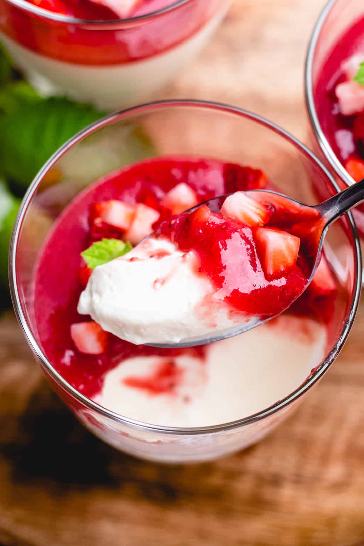 Scooping out panna cotta with strawberry sauce with a spoon from a glass.