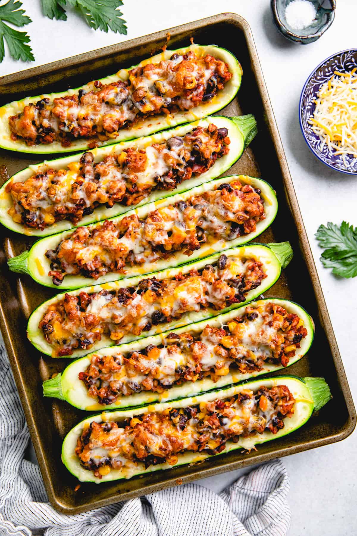 Zucchini boats, stuffed with ground turkey, black beans, and corn, topped with melted cheese on a baking sheet.