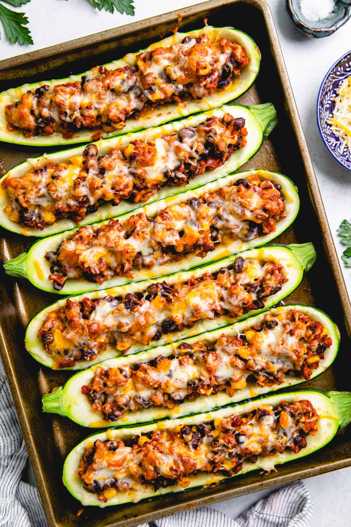 Zucchini boats, stuffed with ground turkey, black beans, and corn, topped with melted cheese on a baking sheet.