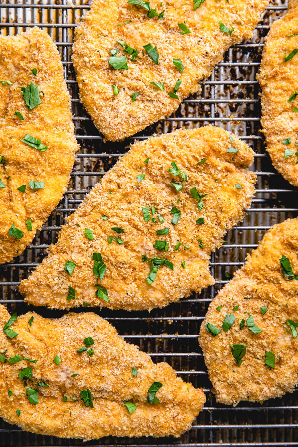 Baked chicken Cutlets topped with chopped parsley on a wire rack.