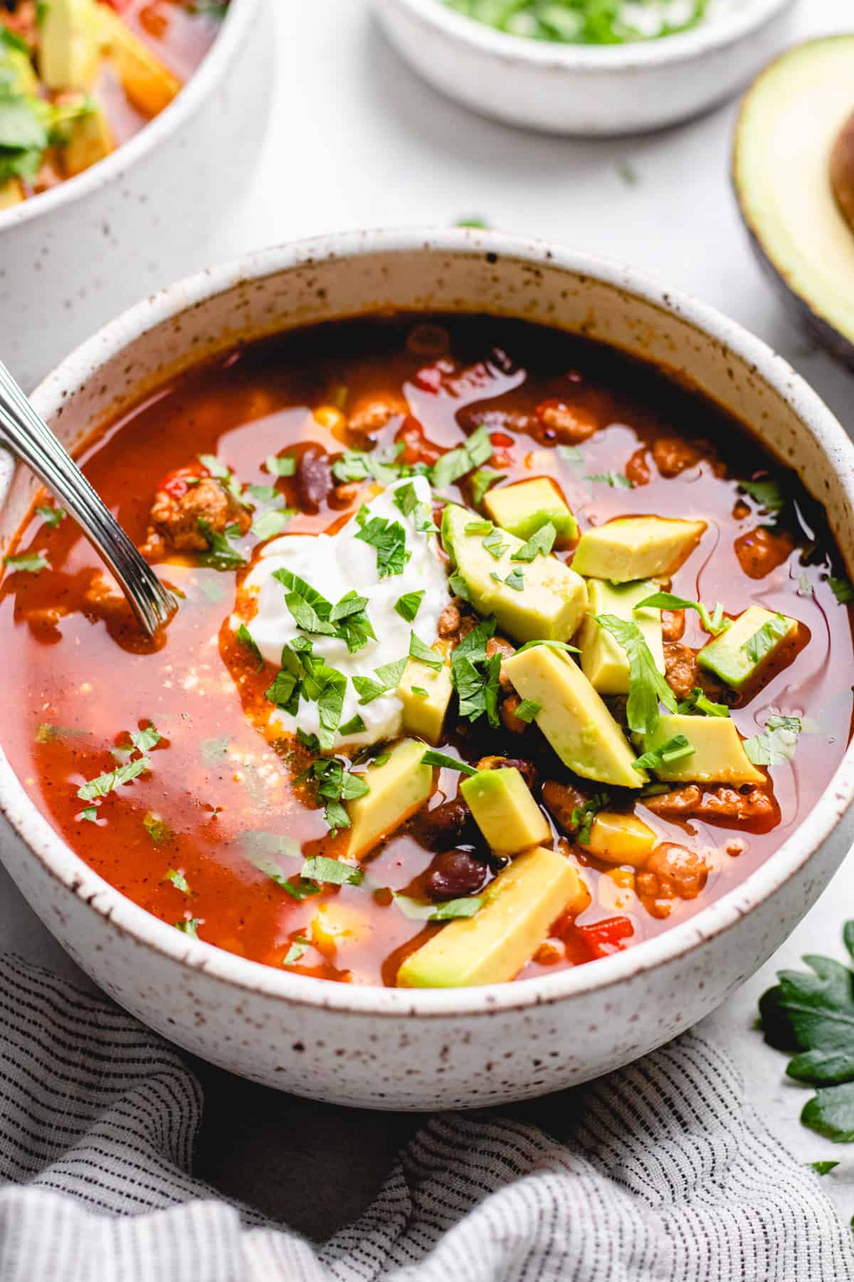 Taco Soup, topped with sour cream, avocado, and cilantro, in a white bowl.