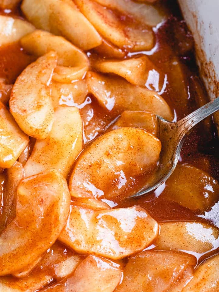 Cinnamon Baked Apples in caramelized sauce in white baking dish.