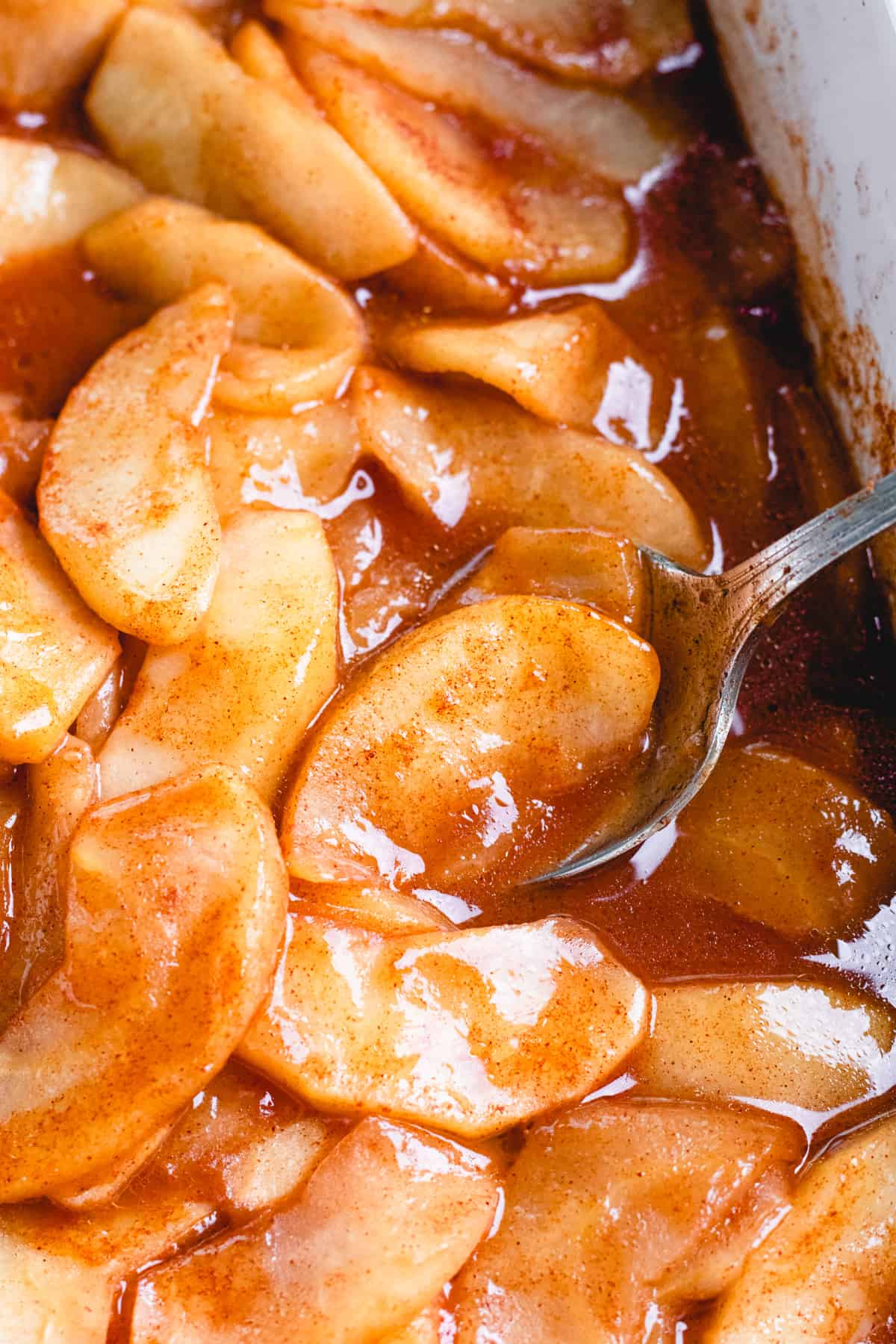 Cinnamon Baked Apples in caramelized sauce in white baking dish.