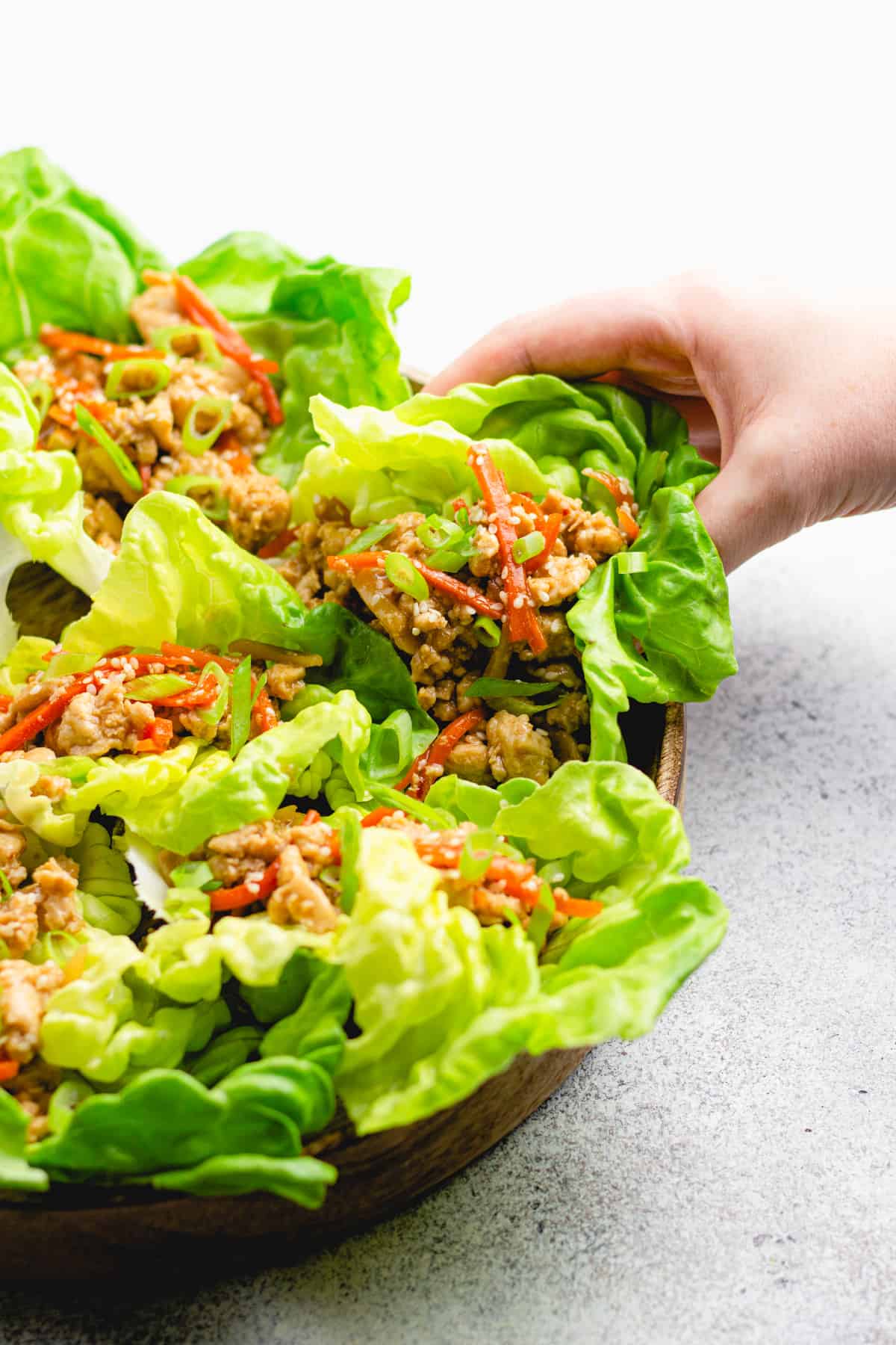 a hand is grabbing a lettuce wrap from a wooden plate.