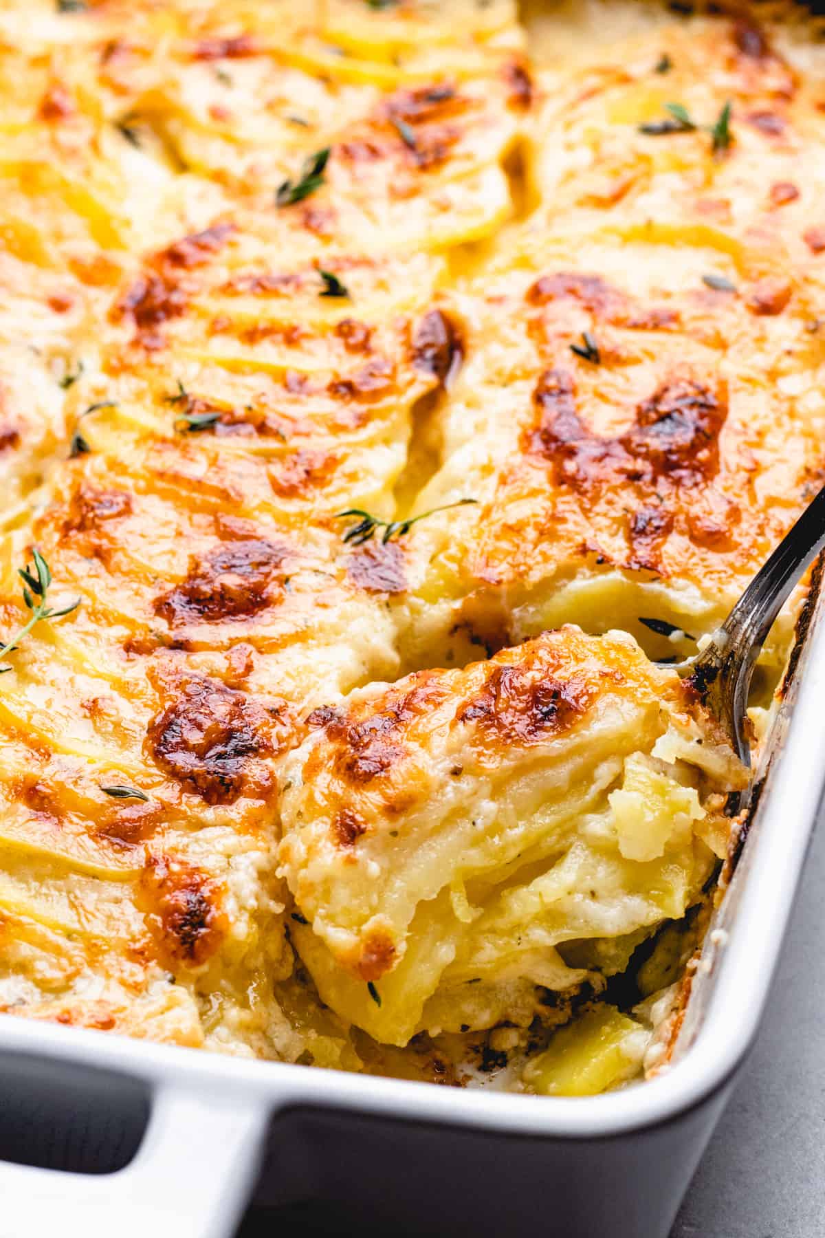 Gruyere Potatoes Au Gratin wiht a cheesy golden brown top in a white casserole with a spoon.