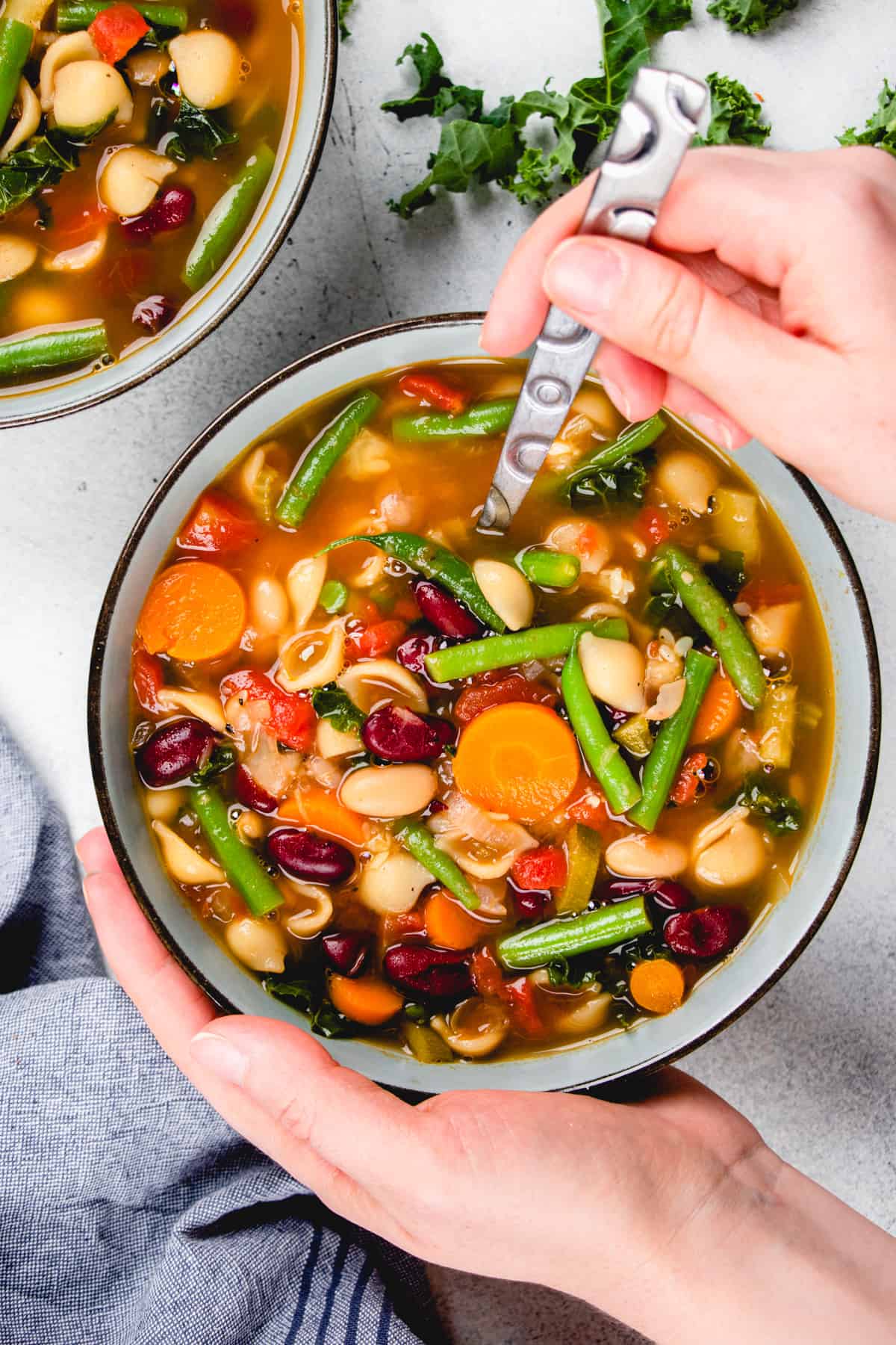 Minestrone soup wit beans, carrots, green beans, pasta in a blue bowl.