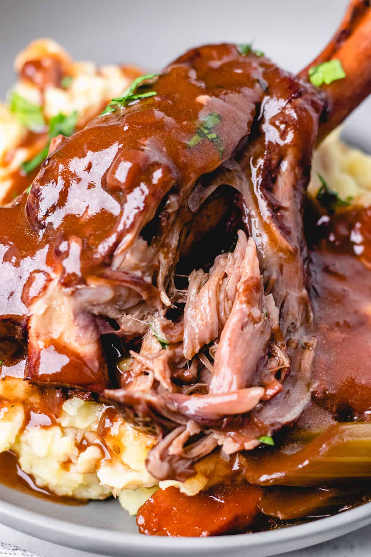 Lamb shank with gravy, vegetables, amd mashed potatoes in a grey bowl.