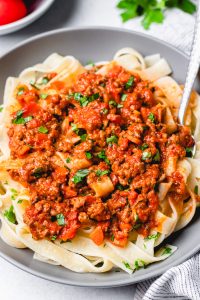 Bolognese sauce over pasta in a grey bowl.