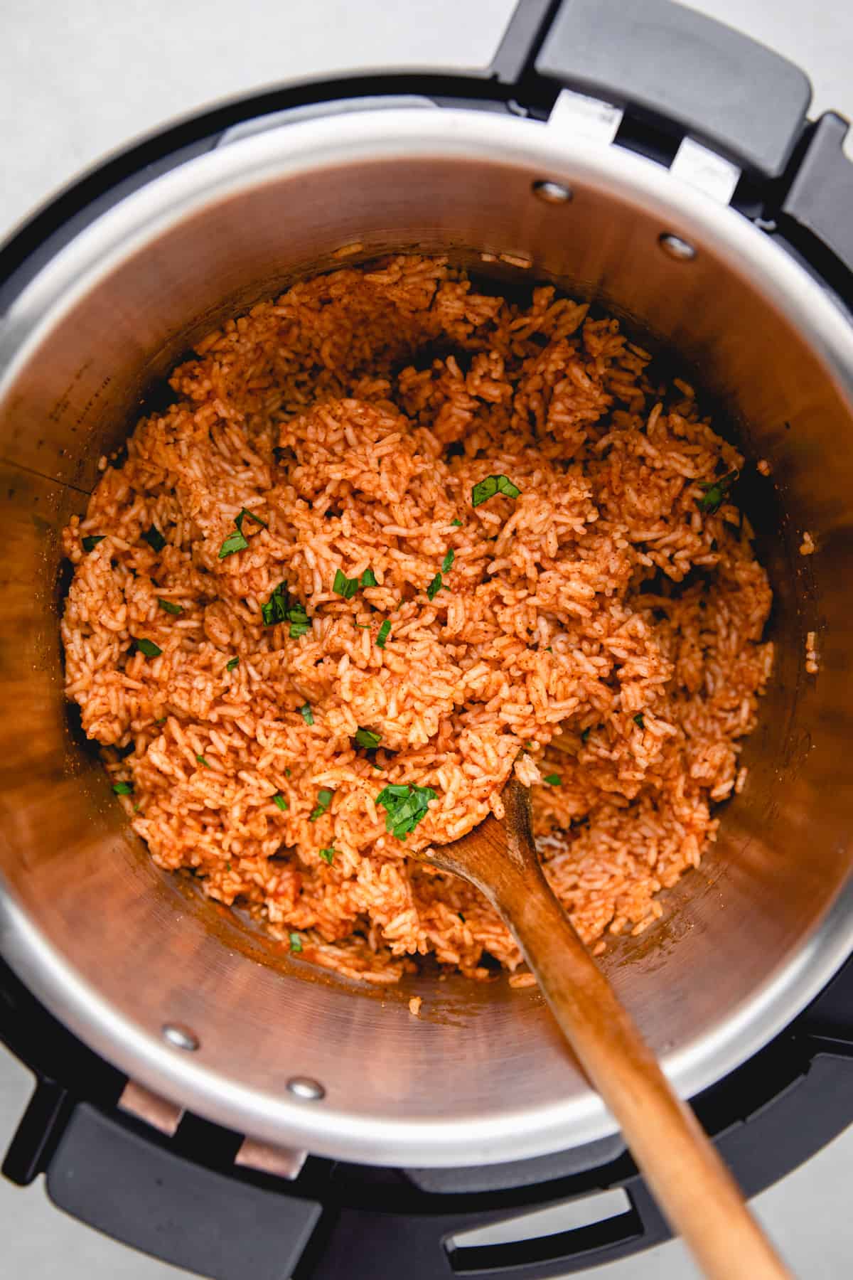 Mexican rice in instant pot, with a wooden spoon and chopped parsley.
