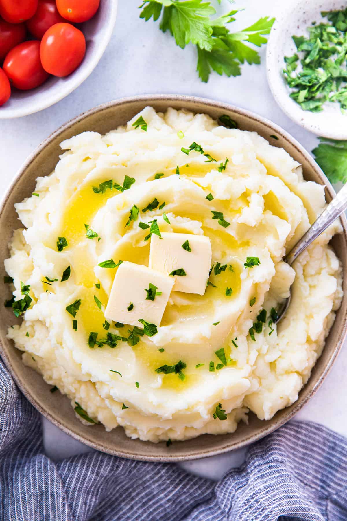 Mashed potatoes, topped with butter and parsley in a bowl with a spoon.