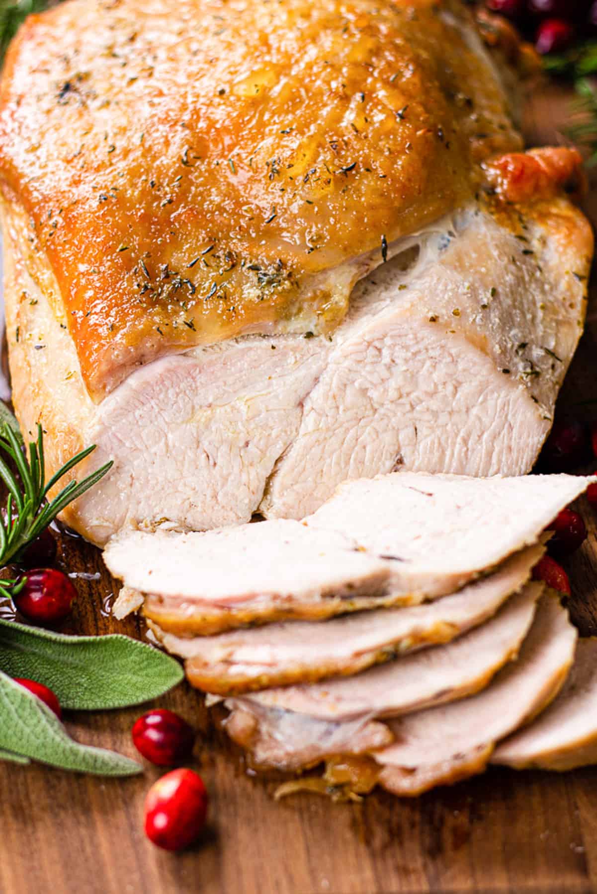 Sliced turkey breast on a cutting board with sage, rosemarin, and cranberries.