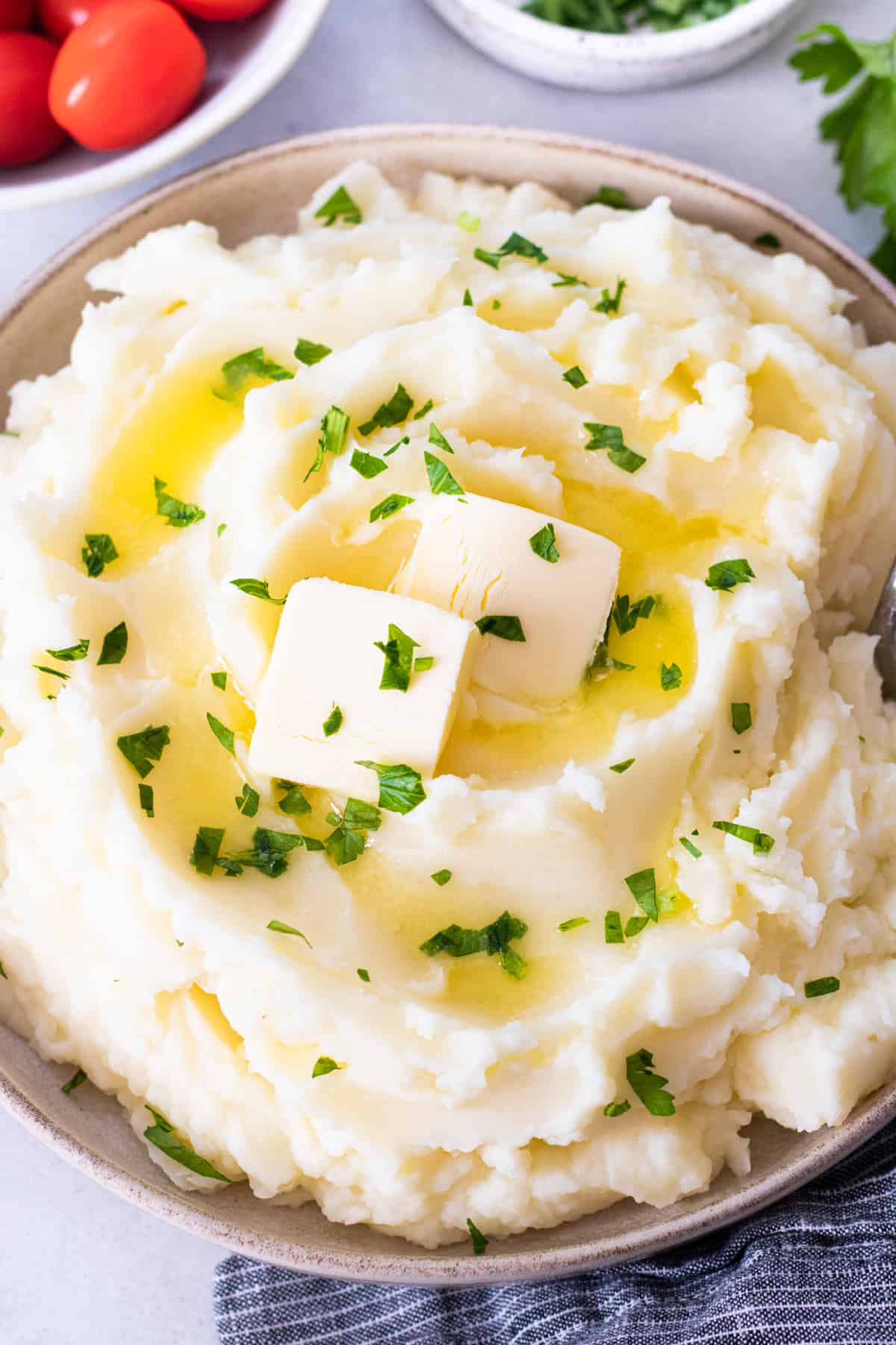 Mashed potatoes, topped with butter and chopped parsley in a bowl.