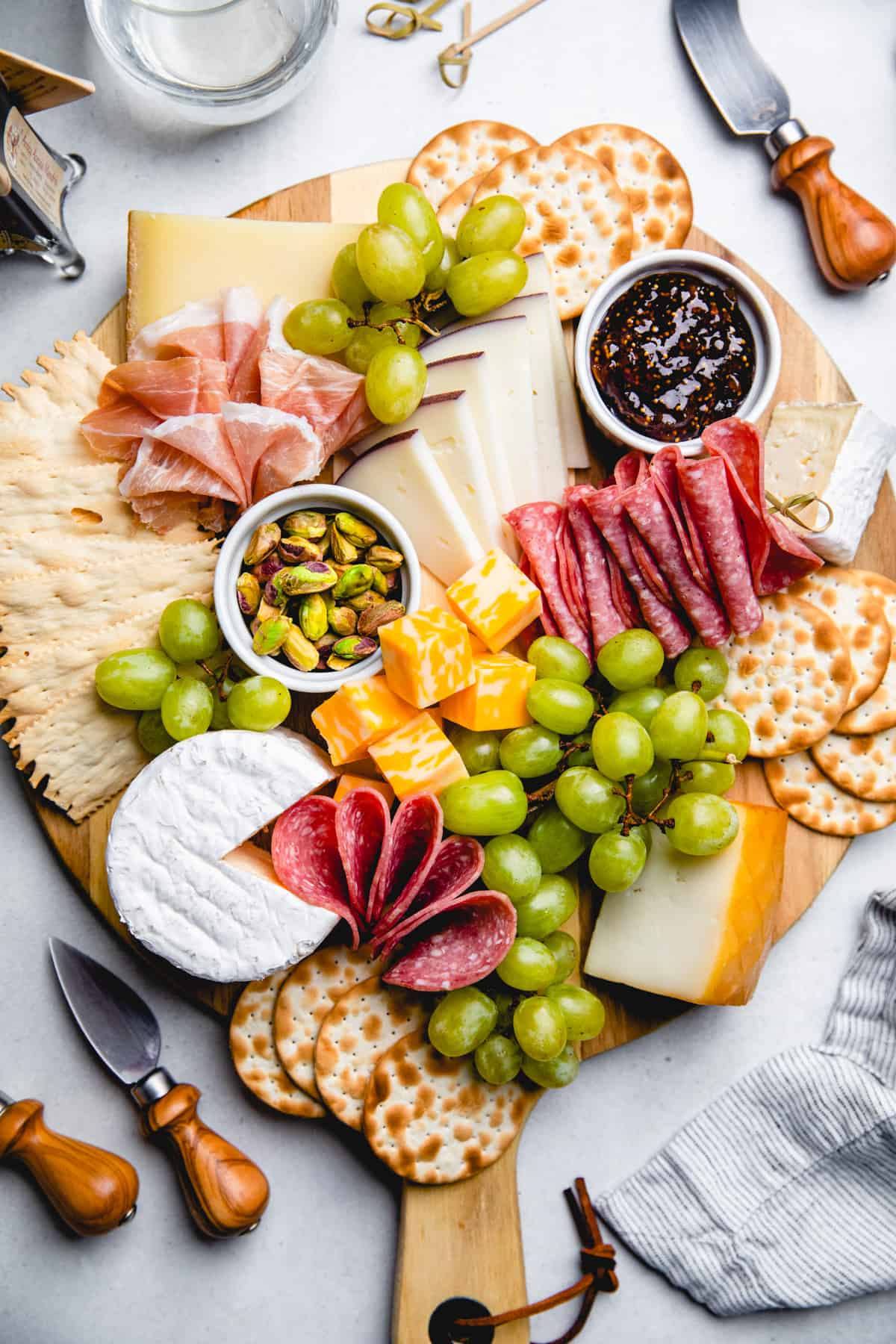 A serving board, topped with cured meats, cheese, crackers, grapes, nuts, and jam.