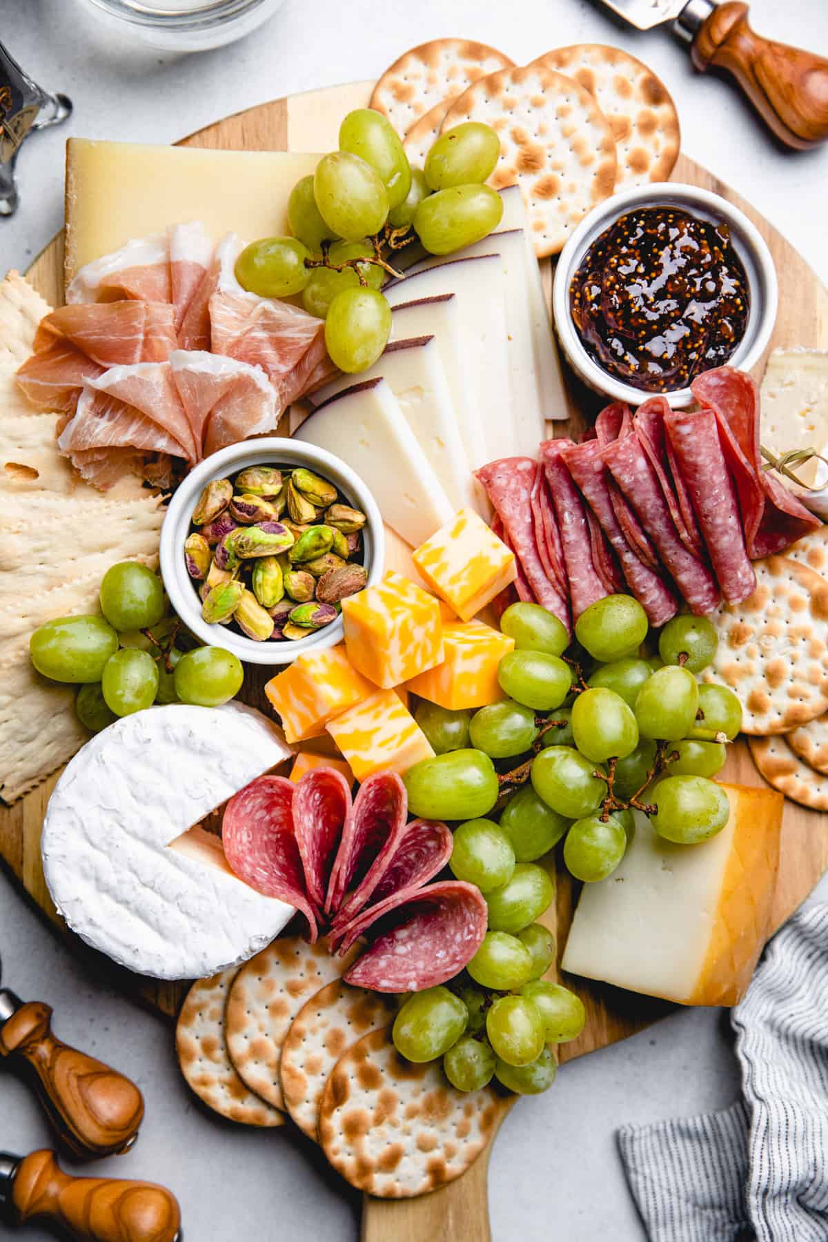 A serving board, topped with cured meats, cheese, crackers, grapes, nuts, and jam.
