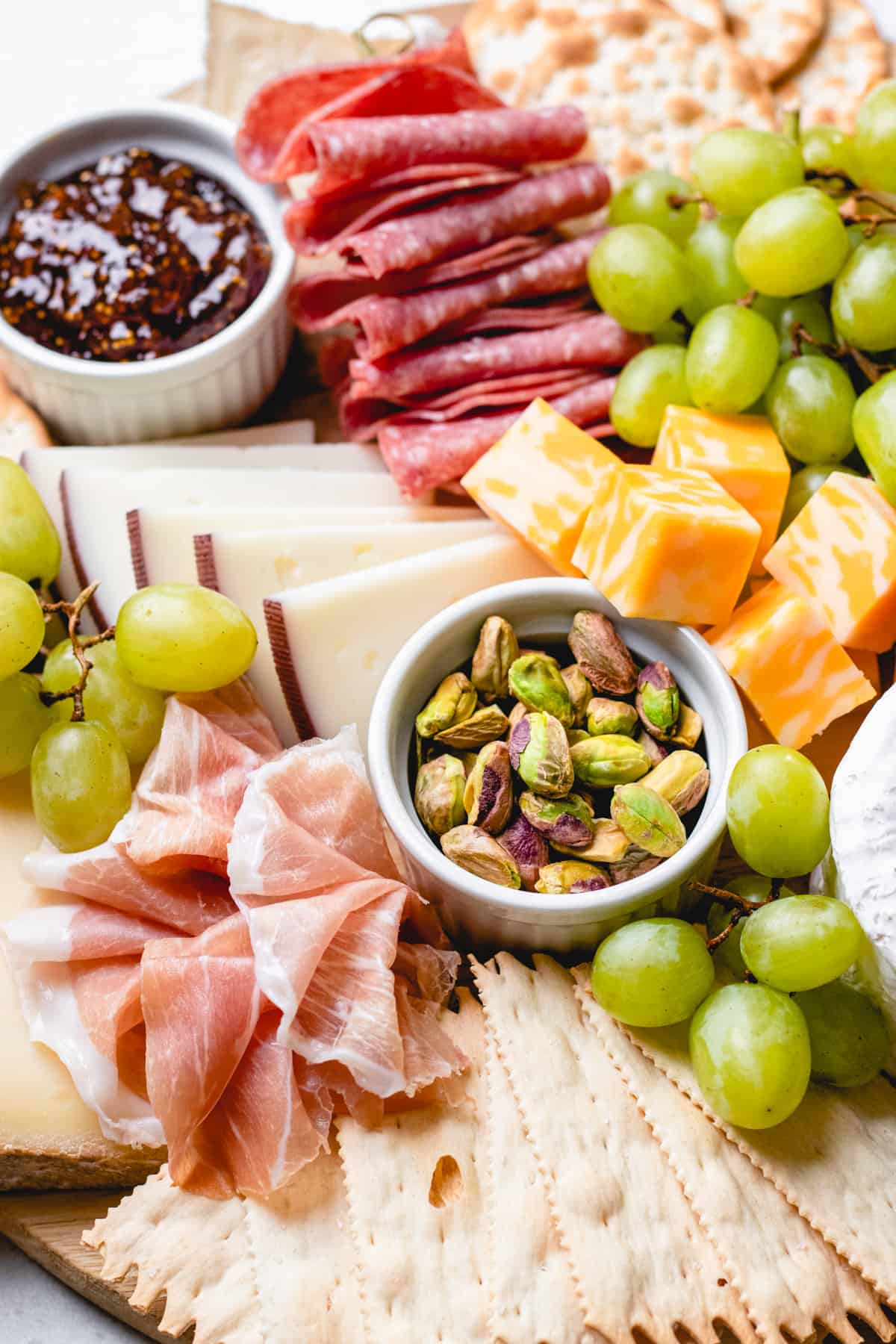 A serving board, topped with cured meats, cheese, crackers, grapes, nuts, and jam.
