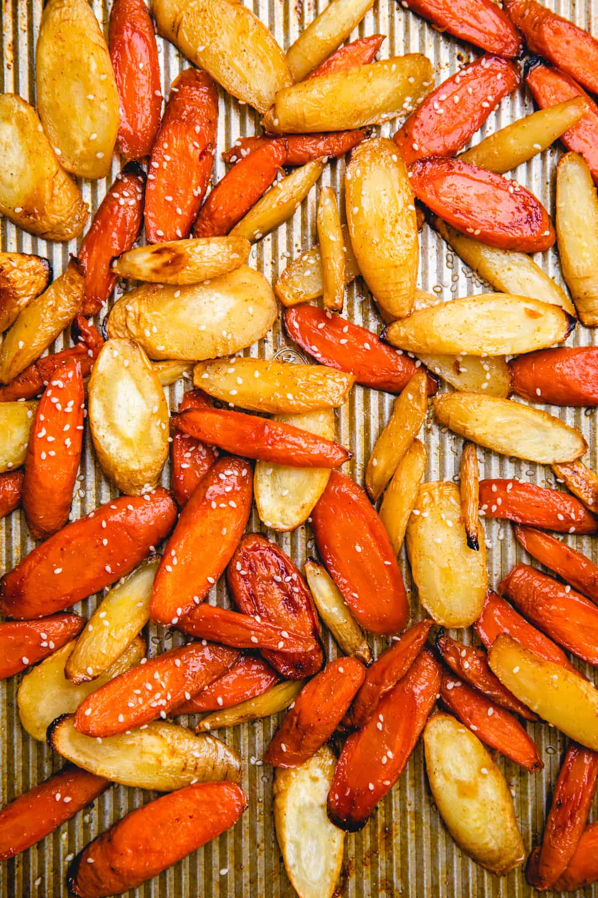 Baked carrots and parsnips on a baking sheet, topped with sesame seeds.