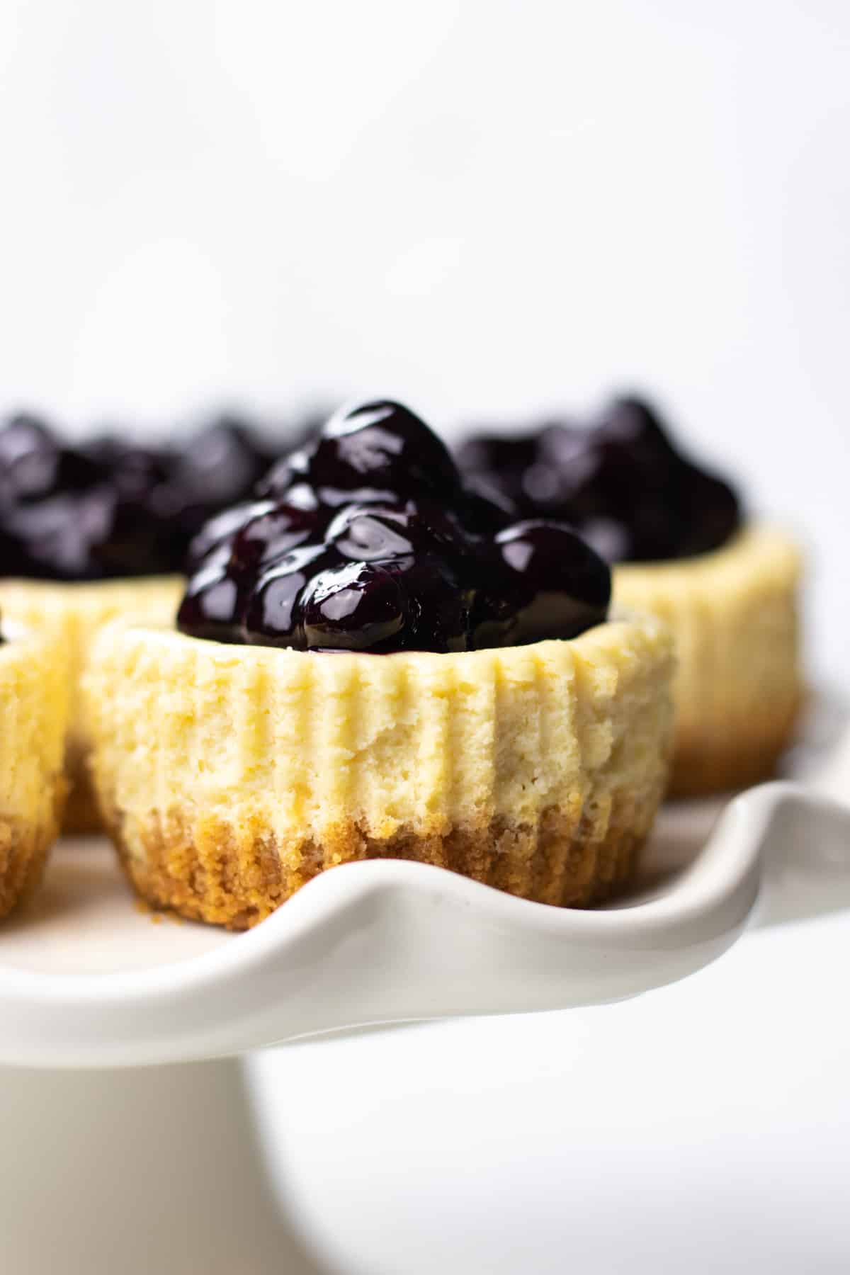 Mini cheesecakes, topped with blueberry sauce, on a cake stand.