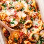 Tortellini with meat sauce and melted cheese in a baking dish with a wooden spoon.