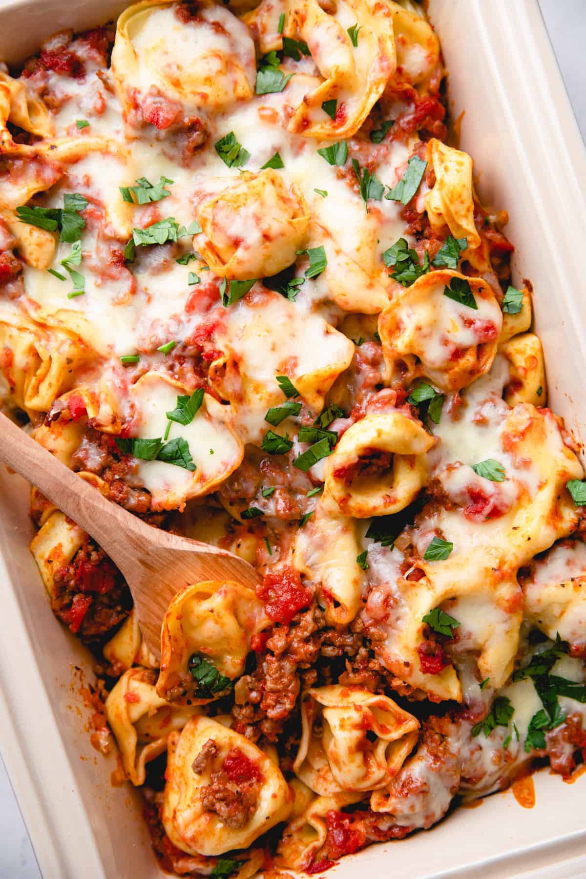 Tortellini with meat sauce and melted cheese in a baking dish with a wooden spoon.