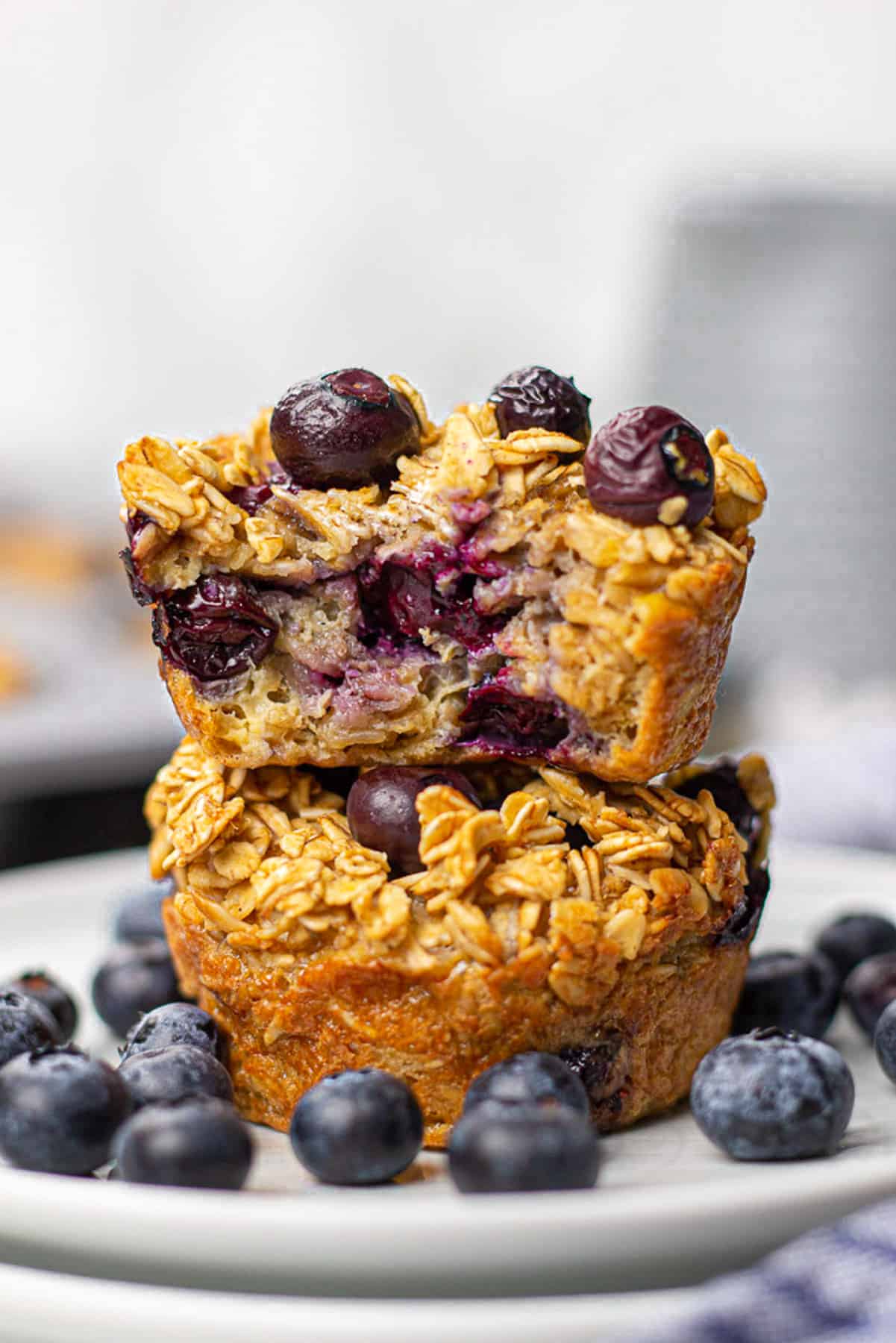 Blueberry Baked Oatmeal Cups on top of each other on a plate with blueberries around them.