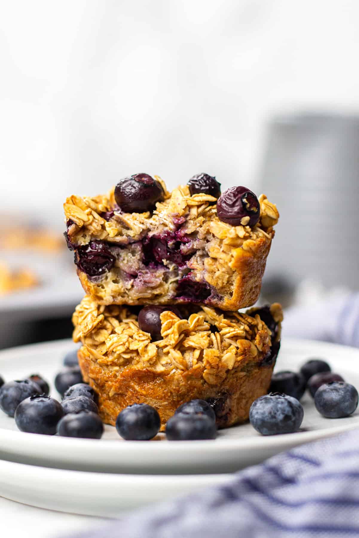 Blueberry Baked Oatmeal Cups on top of each other on a plate with blueberries around them.