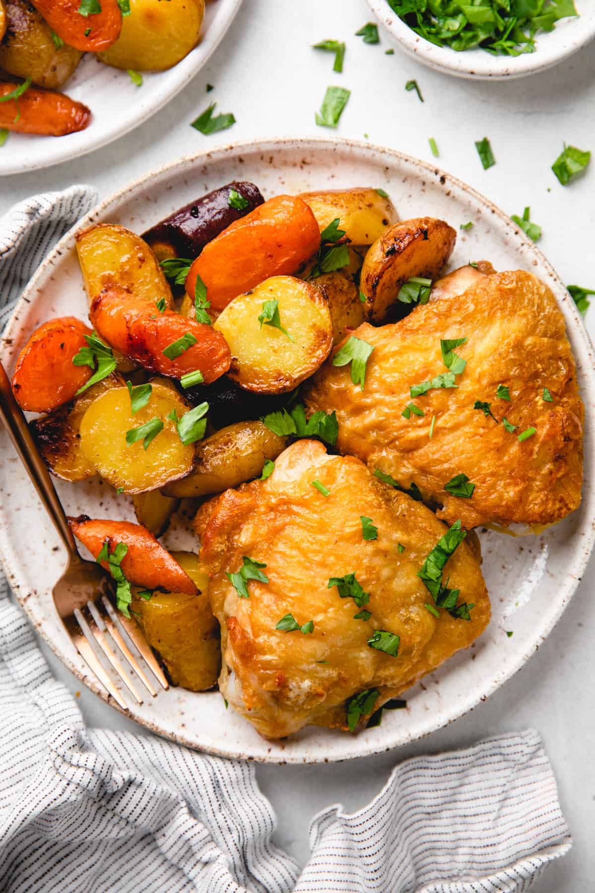 Roasted chicken thighs with carrots and potatoes on a plate.