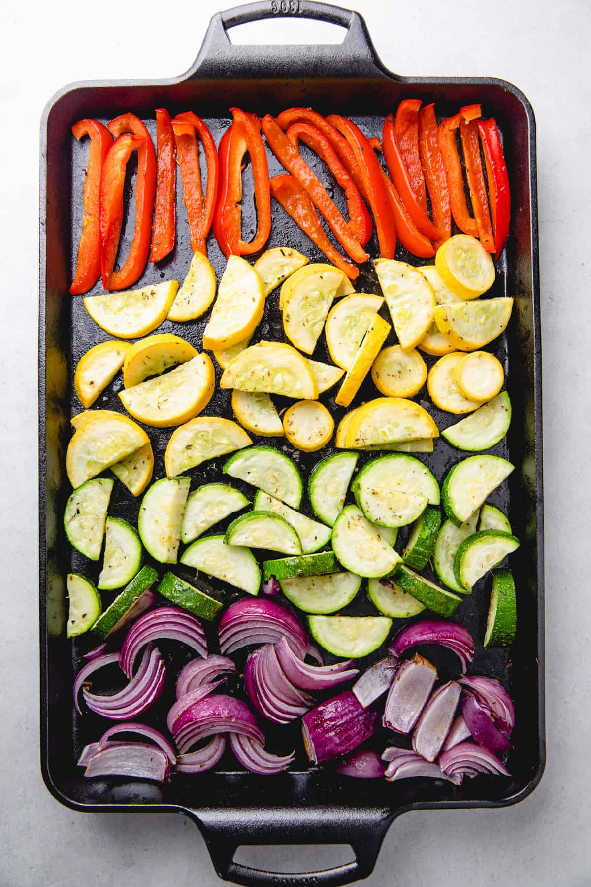 Diced red bell pepper, red onion, zucchini, and yellow squash on a baking sheet.