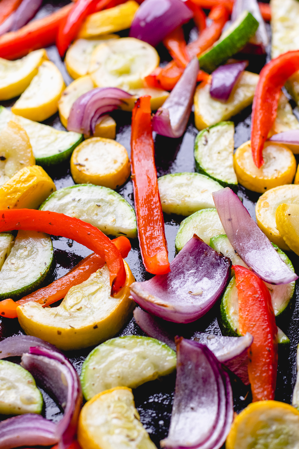 Roasted red bell pepper, red onion, zucchini, and yellow squash on a baking sheet.
