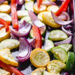 Roasted red bell pepper, red onion, zucchini, and yellow squash on a baking sheet.
