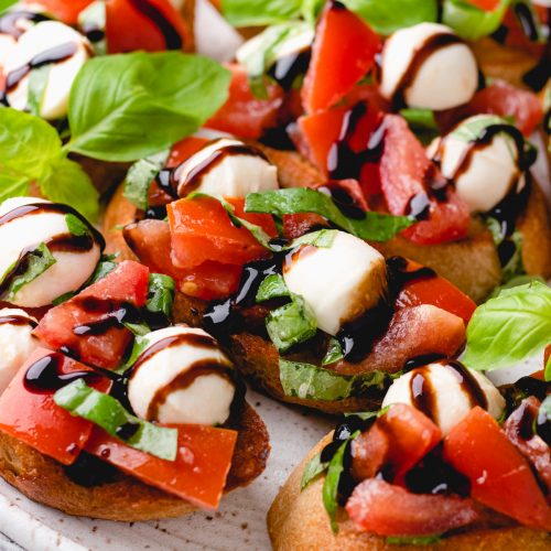 Bread slices, topped with diced tomatoes, mozzarella, and basil, and drizzled with balsamic glaze.