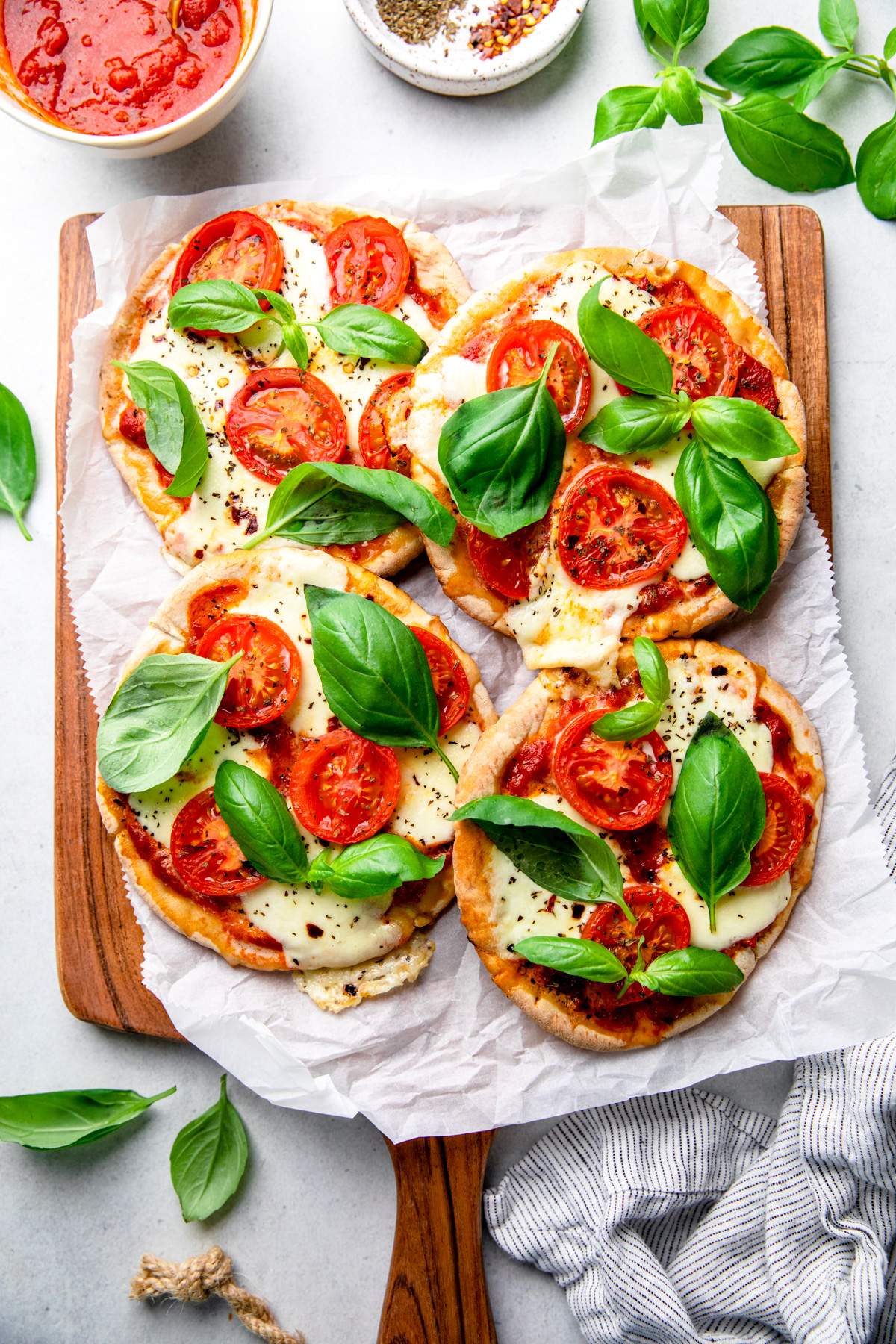 Mini Margherita pizza made with pita bread, topped with cheese, tomatoes, and basil on a cutting board.
