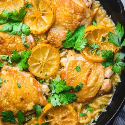 Chicken thighs with orzo and lemon slices in a skillet.