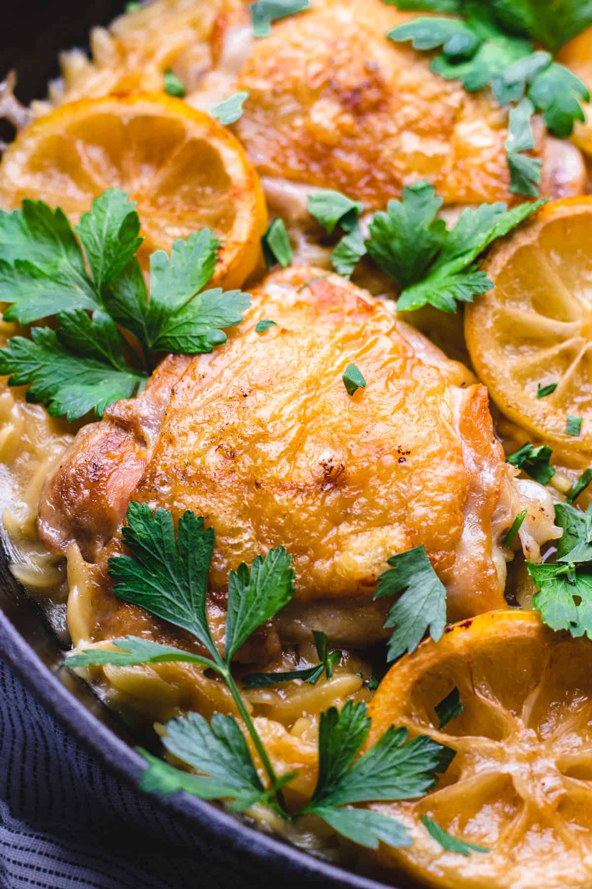 Chicken thighs with orzo and lemon slices in a skillet.