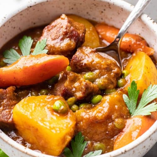 Stew with beef tips, potatoes, carrots, and peas in a bowl.