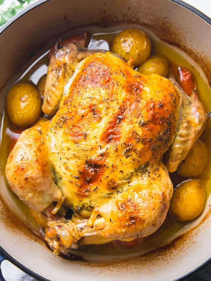 Whole roasted chicken in a Dutch oven with potatoes and carrots.