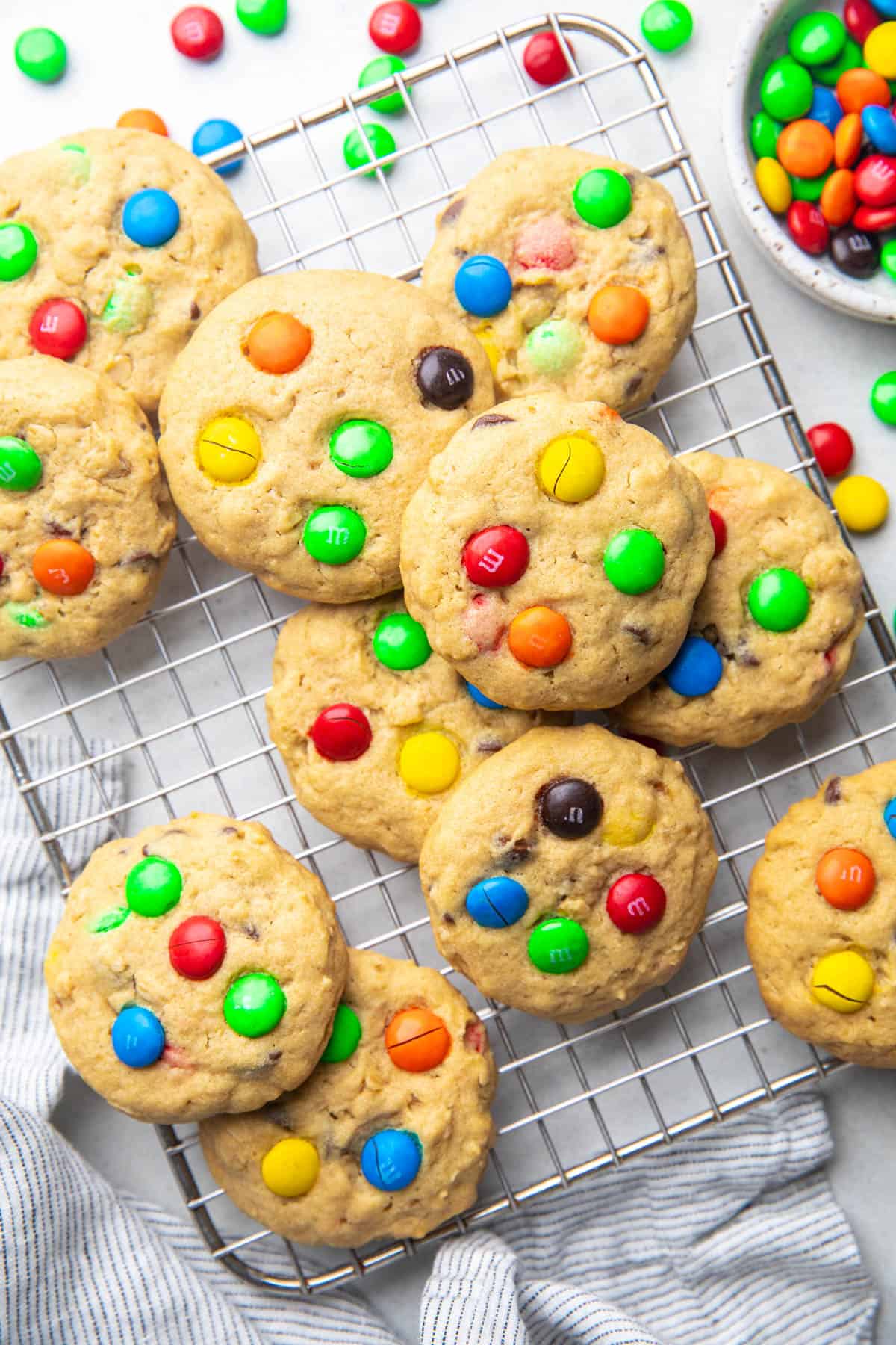 Cookies topped with M&Ms and chocolate chips on a wire rack.