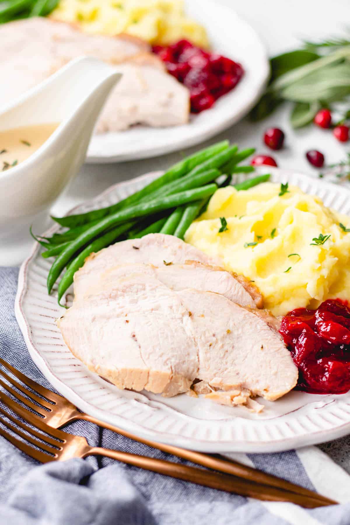 Slices ob turkey meat, mashed potatoes, green beans, and cranberry sauce on a plate.