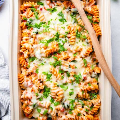 Pasta with chicken, spinach, with blush sauce, topped with melted cheese and parsley, in a baking dish.
