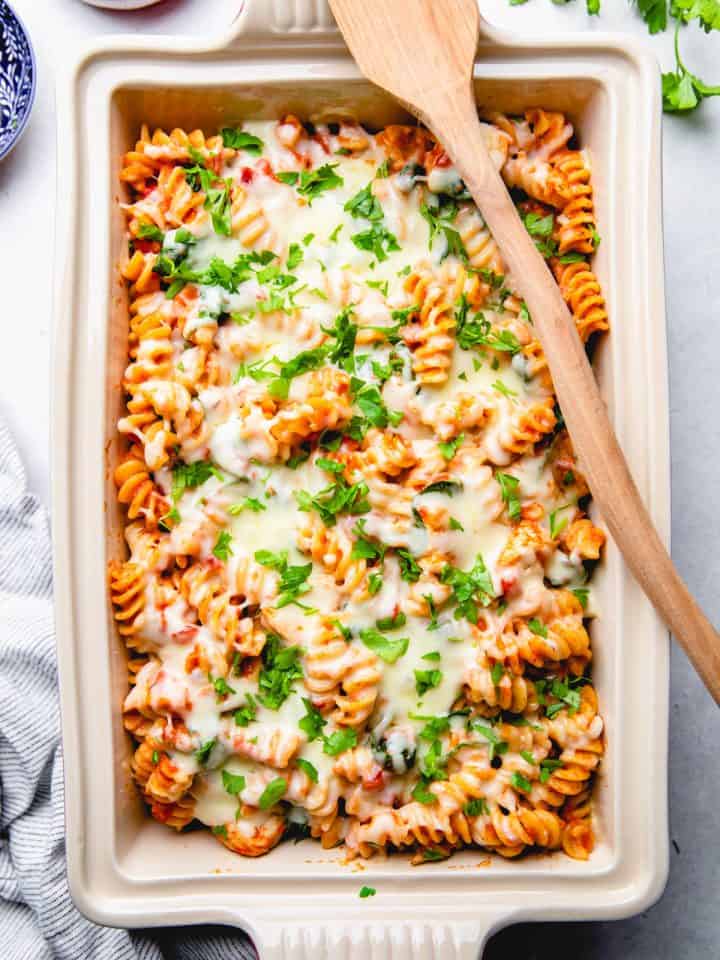 Pasta with chicken, spinach, with blush sauce, topped with melted cheese and parsley, in a baking dish.