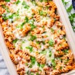 Pasta with chicken, spinach, with blush sauce, topped with melted cheese and parsley, in a baking dish.