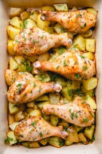 Chicken drumsticks with potatoes in a baking dish.